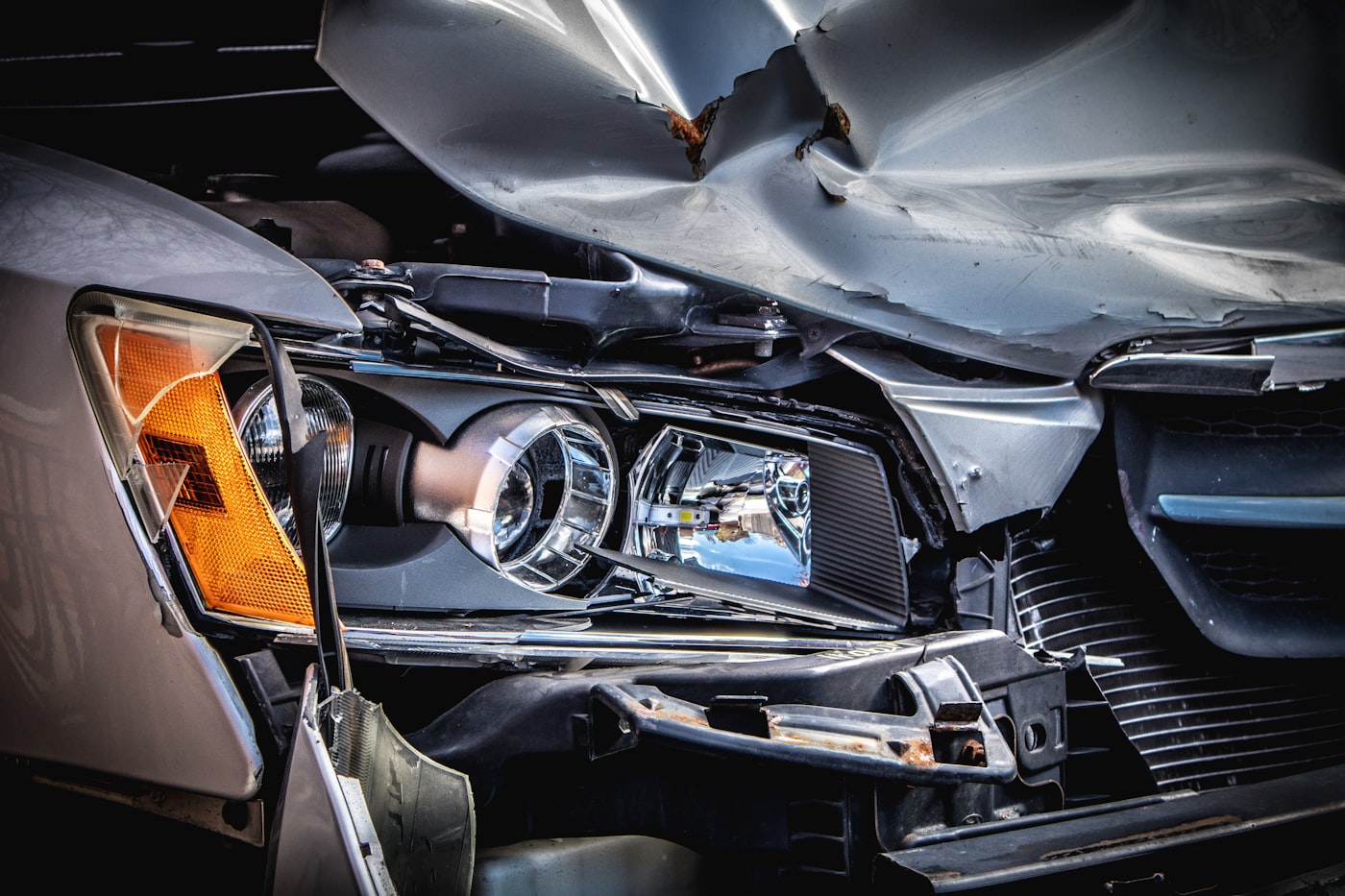 A silver car with a crushed hood and broken headlight after a collision
